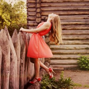 Woman in Orange Sleeveless Flare Dress Standing in Front of Wooden Fence