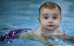 Cute Baby Is Swimming On Body Of Water Wearing Purple Shorts In A Blur Water Background HD Cute