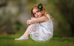 Cute Girl Baby Is Wearing White Dress Sitting On Grass Facing One Side And Having Green Leaves On Head In A Blur Background HD Cute HD Wallpaper