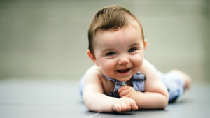 Cute Smiley Baby Is Lying Down On Floor Wearing Light Blue Dress In A Blur Background HD Cute