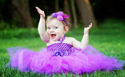 Cute Smiley Girl Baby Is Sitting On Green Grass Wearing Purple Frock And Flower Band On Head Having Hands In The Air HD Cute