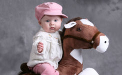Cute Baby Is Sitting On Toy Horse Wearing White Top And Pink Pant And Cap In Ash Background HD Cute