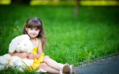 Cute Little Girl Is Wearing Yellow Dress Sitting On Green Grass In Blur Green Background With Teddy Toy HD Cute