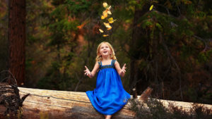 Little Cute Girl Is Sitting On Tree Trunk Wearing Blue Dress Looking Up HD Cute