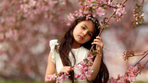Cute Ash Eyes Little Girl Is Touching Blossom Branch Pink Flower Wearing White Dress In Blur Flowers Background HD Cute