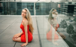 Girl Model With Red Dress And Blonde Hair Is Sitting With Reflection On Glass