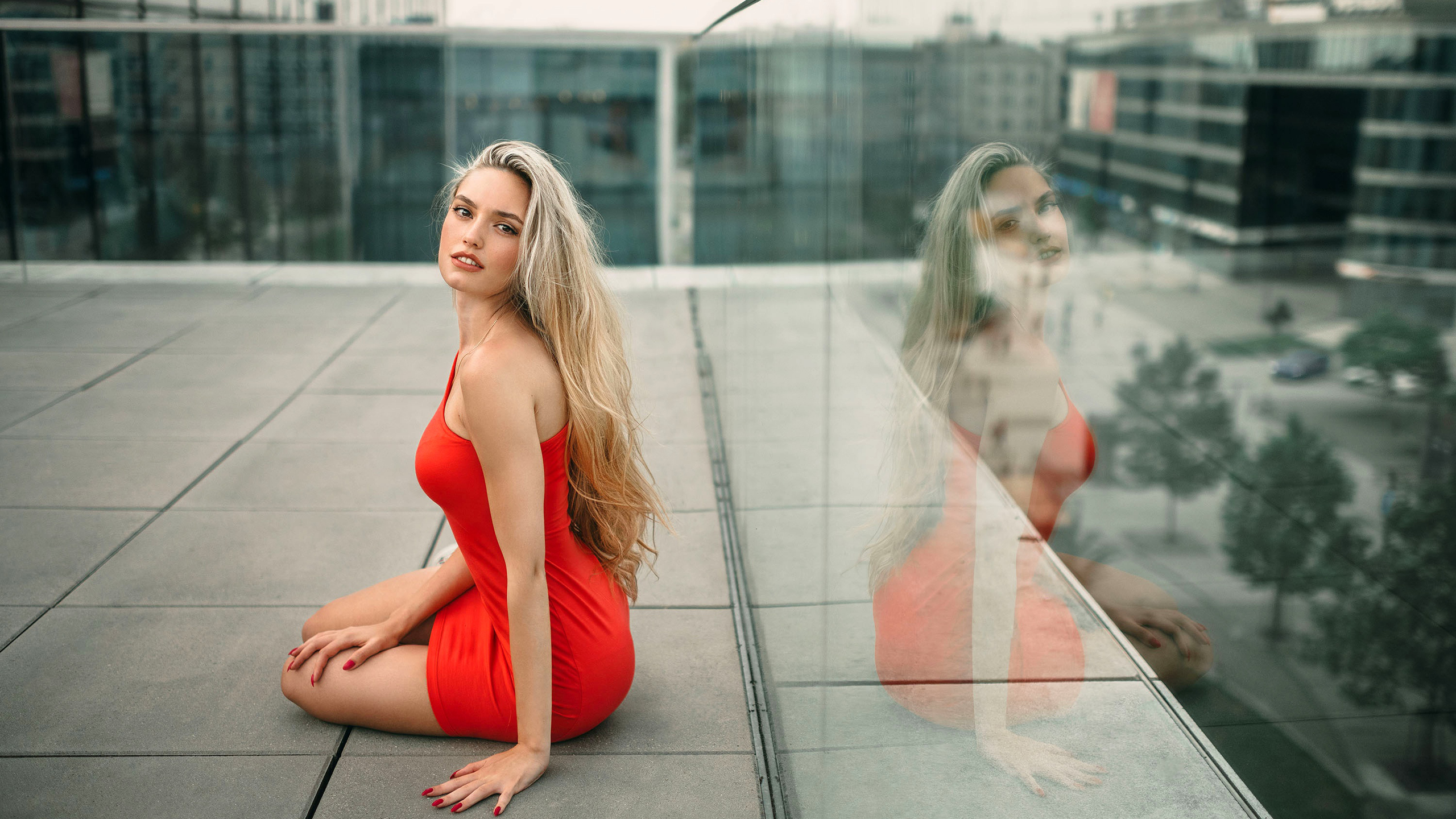 Girl Model With Red Dress And Blonde Hair Is Sitting With Reflection On Glass