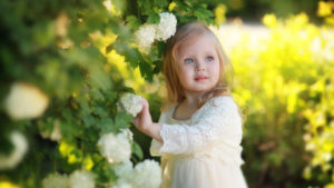 Little Cute Ash Eyes Girl Is Wearing White Netted Dress Standing Near Green Plant Touching White Flower HD Cute