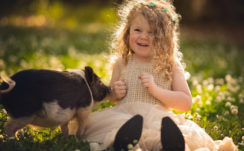 Beautiful Curly Hair Smiling Cute Little Girl Is Sitting On Grass Near Pig Wearing Light Peach Color Dress HD Cute Wallpapers