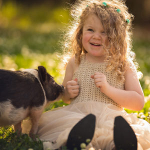 Beautiful Curly Hair Smiling Cute Little Girl Is Sitting On Grass Near Pig Wearing Light Peach Color Dress HD Cute Wallpapers